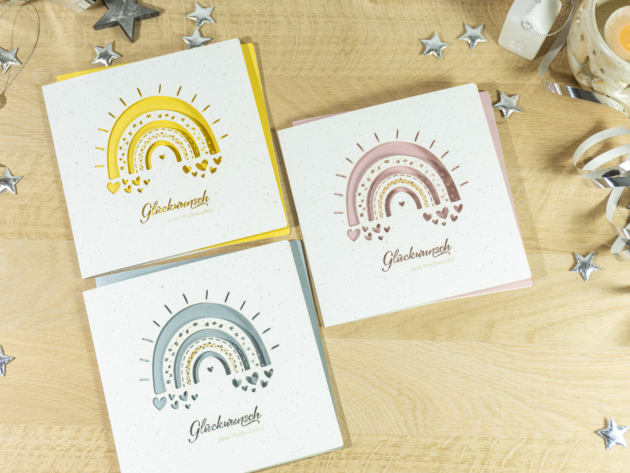 PALUXA_Babyglueck_mit_Regenbogen_3_Varianten_birdview.jpg Drei Farbvarianten PALUXA Lasercut-Babykarte mit Regenbogen-Motiv, liegend.