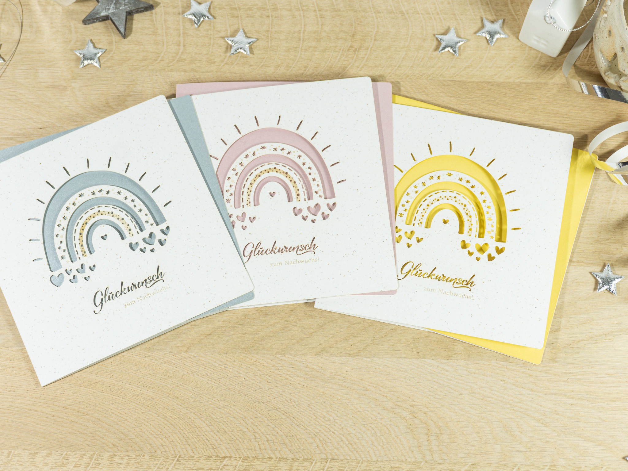 PALUXA_Babyglueck_mit_Regenbogen_3_Varianten.jpg Drei Farbvarianten PALUXA Lasercut-Babykarte mit Regenbogen Motiv, liegend.