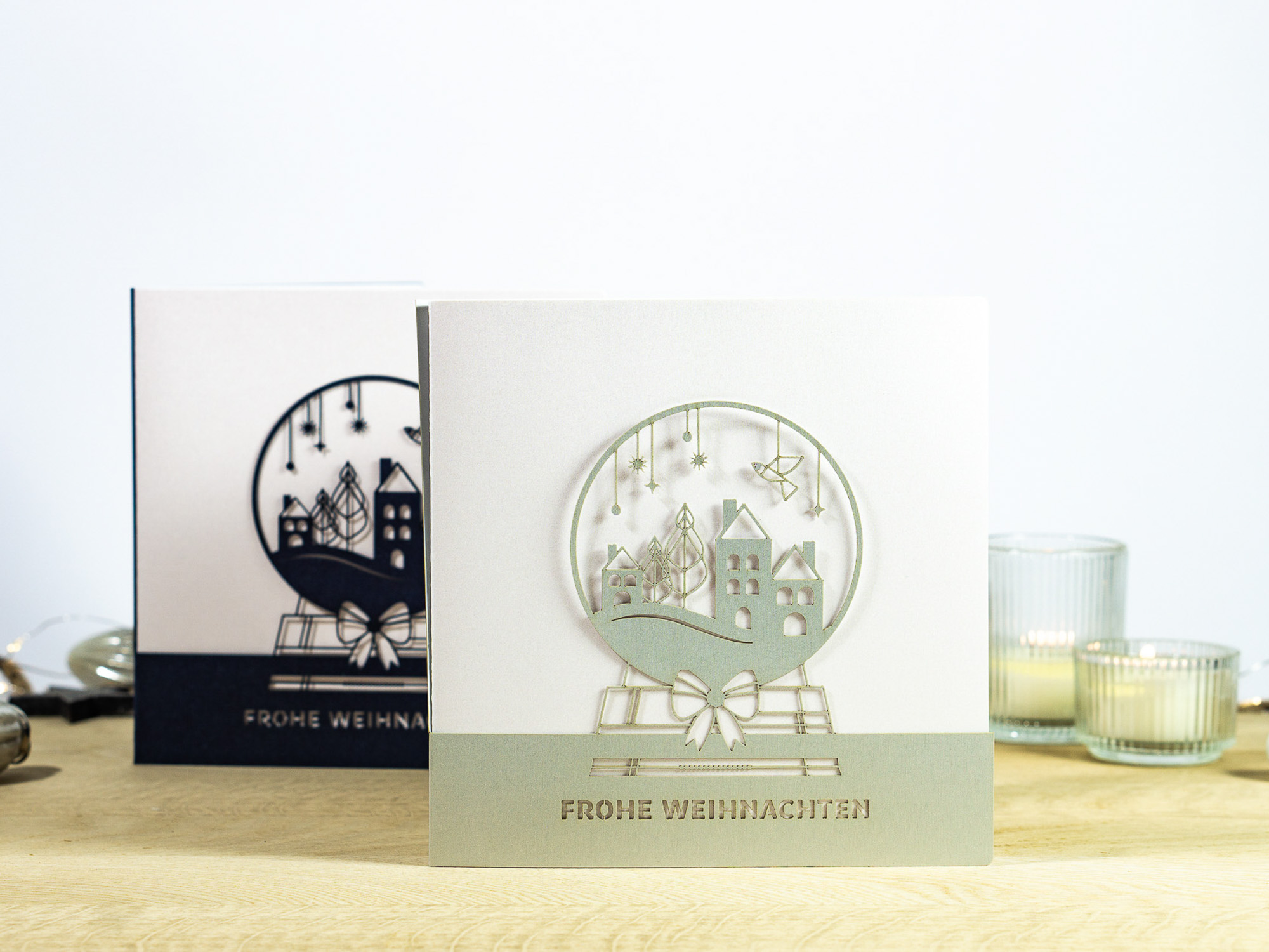 Zwei Farbvarianten PALUXA Lasercut-Weihnachtskarte mit Schneekugel Motiv, stehend, in Farbe Silber und Nachtblau.